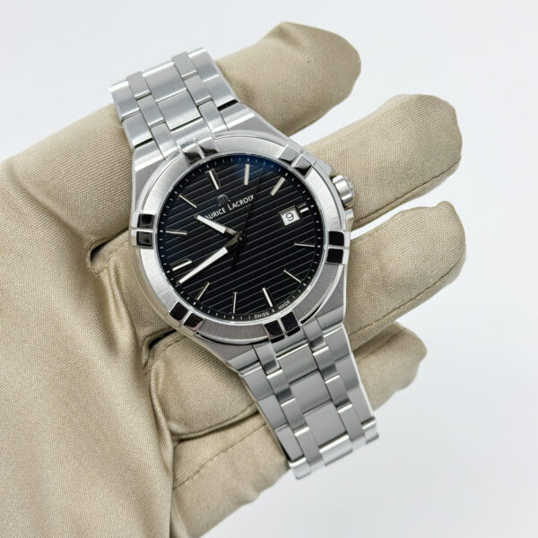 Maurice Lacroix Aikon Ref. AI1008 wristwatch with black striped dial and stainless steel bracelet, displayed in a gloved hand