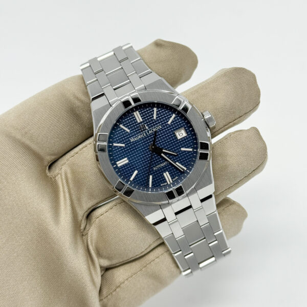 Maurice Lacroix Aikon automatic watch with blue textured dial and stainless steel bracelet, shown held in a gloved hand