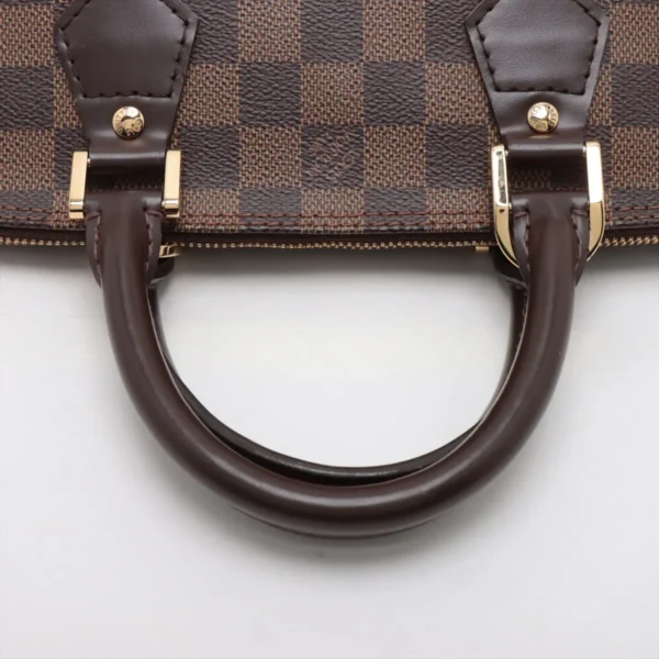 Close-up of the rolled leather handles and gold-tone hardware attached to the checkered canvas.