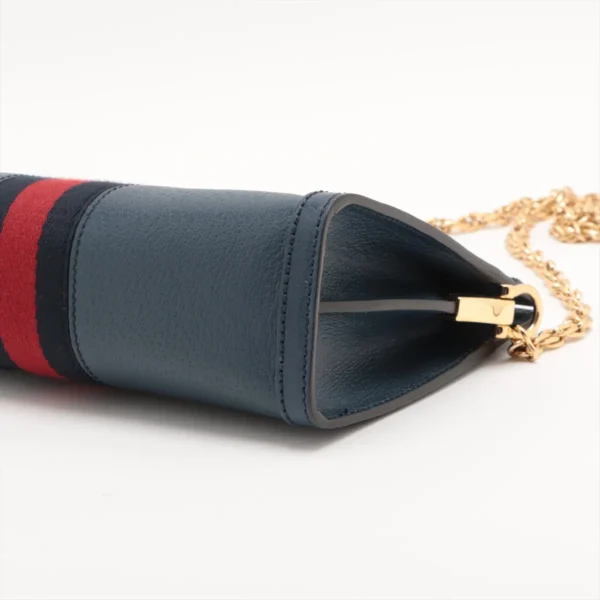 Close-up side view of a dark blue leather bag with a red and navy fabric stripe, featuring a gold chain strap and gold hardware on a white background.