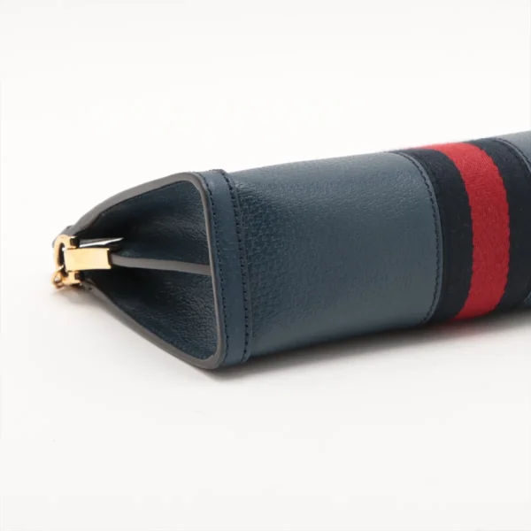 Close-up of the side of a dark blue leather bag with a red and black fabric stripe and a gold clasp on a white background