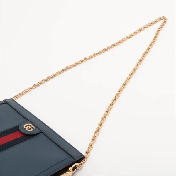 Close-up of a blue handbag with a gold-colored GG logo and a red and blue stripe detail, featuring a gold chain strap on a white background.
