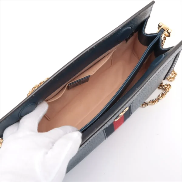 Top view of an open blue handbag with a beige interior, showing the compartments and a white-gloved hand holding the edge of the bag