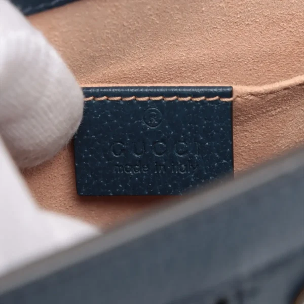 Close-up of a dark blue leather Gucci label stitched on beige suede with the embossed text 'gucci made in italy' and a registered trademark symbol above.