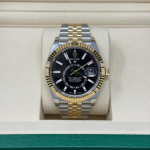 Rolex Sky-Dweller wristwatch with a black dial, gold fluted bezel, and two-tone metal bracelet inside a cream-colored box
