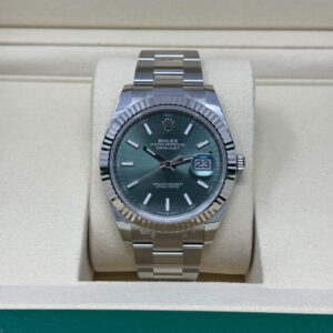 Stainless steel Rolex Datejust with fluted bezel and green sunburst dial showing date "23" on a cream watch cushion