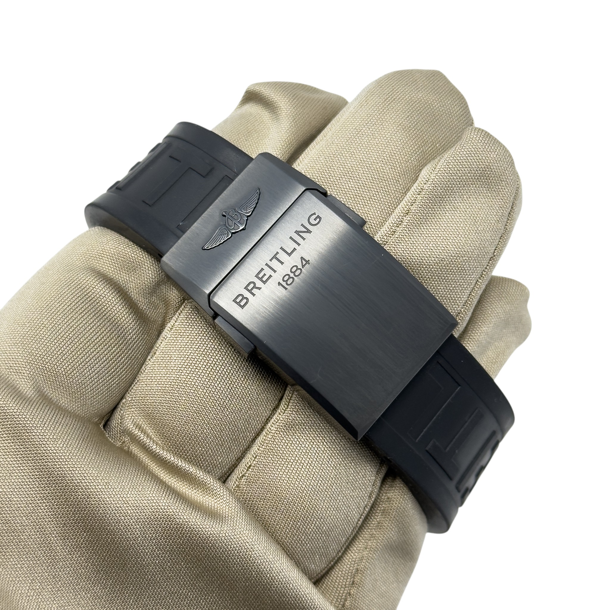 Black Breitling watch clasp held against beige padded fabric, engraved with winged logo and "BREITLING 1884".