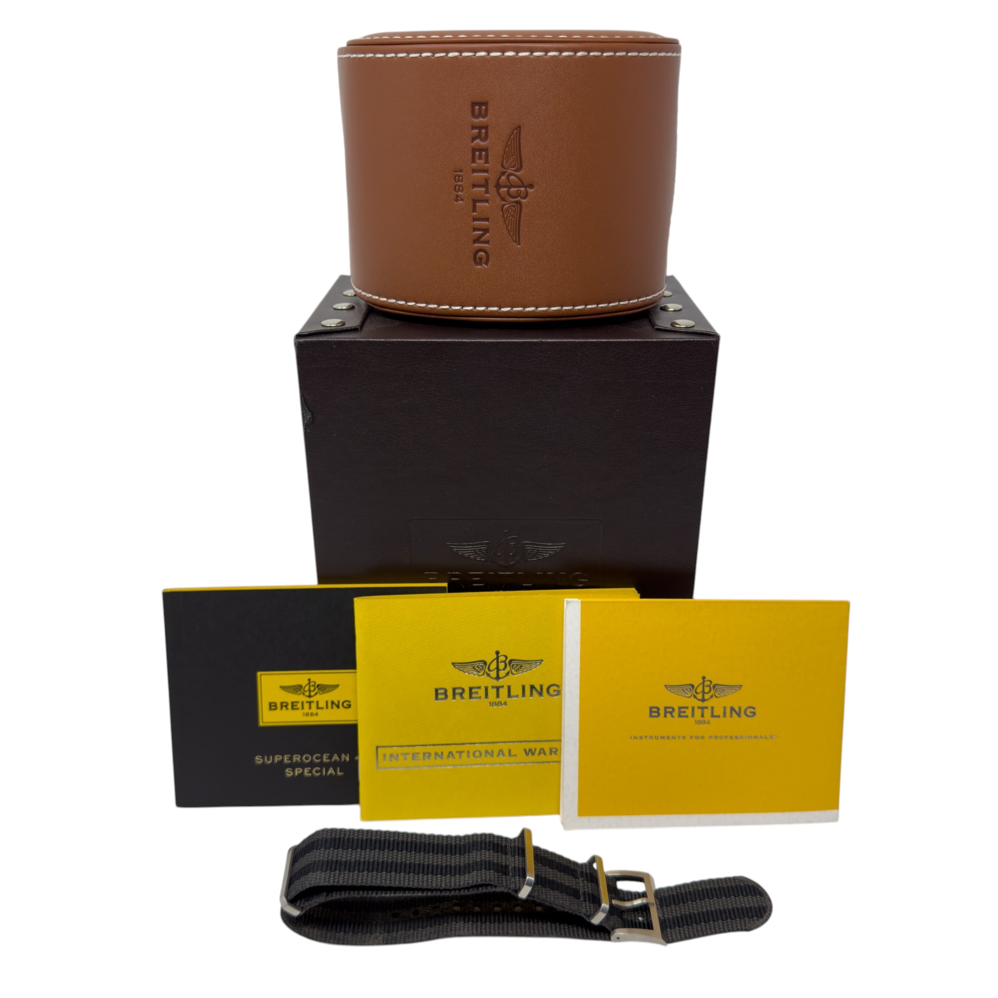 Brown leather Breitling watch case on a dark box with yellow instruction booklets and a black nylon watch strap below